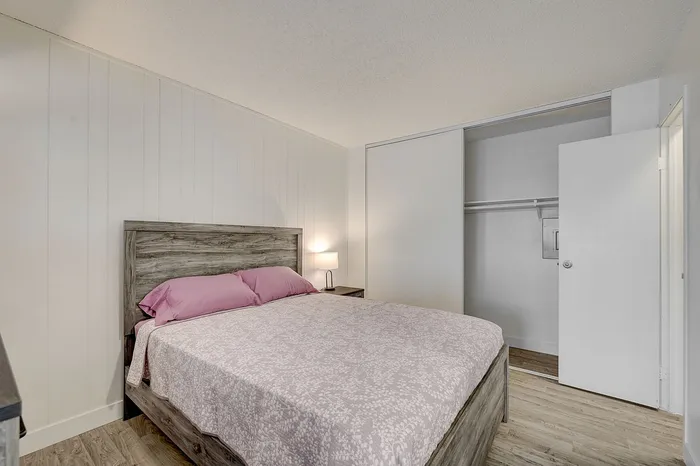 Inviting bedroom with cozy wooden bed frame, soft pink bedding, and spacious sliding closet in modern apartment.