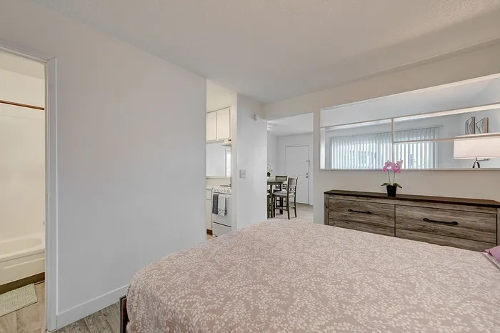 Inviting bedroom with cozy decor, leading to a bright dining area and kitchen; perfect for modern living.