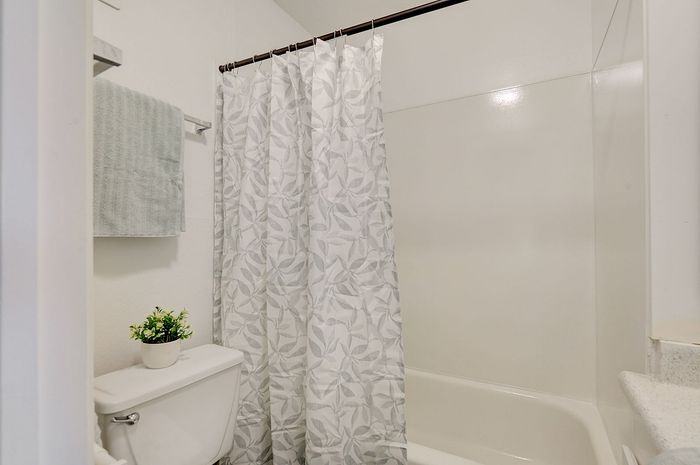 Charming bathroom with elegant leafy shower curtain, cozy towel rack, and a fresh green plant for a rejuvenating atmosphere.