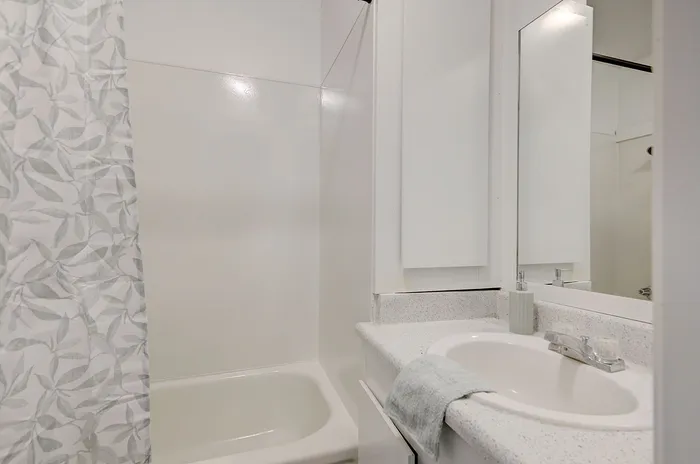 Bright, modern bathroom featuring sleek surfaces, a polished countertop, elegant sink, and a stylish shower curtain with leaf pattern.