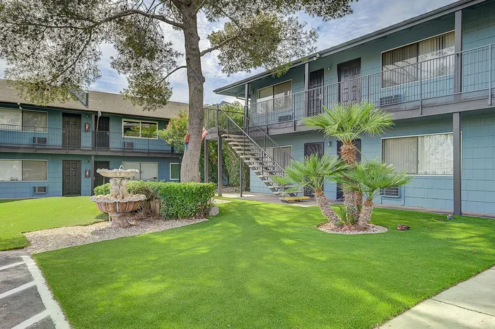 Charming apartment complex with well-maintained greenery, inviting stairway entrance, and a decorative fountain in a serene outdoor setting.