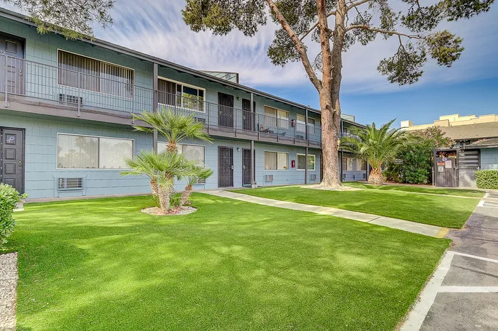 Charming two-story apartment complex with a serene green lawn, mature trees, and inviting balconies for relaxed living.