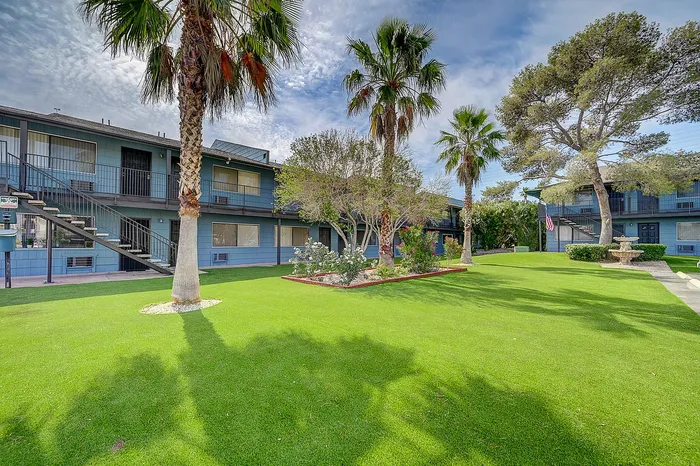 Charming apartment complex with lush green lawn, elegant palm trees, and inviting exterior balconies, offering a serene community atmosphere.