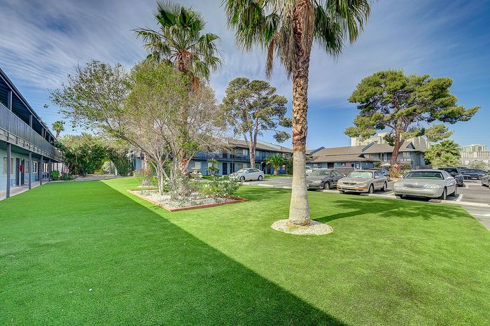 Vibrant apartment complex with lush green lawns, palm trees, and ample parking, offering a serene and inviting atmosphere.