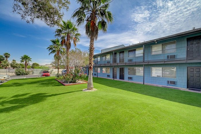 Charming apartment complex featuring lush green lawns and tall palm trees under a clear blue sky.