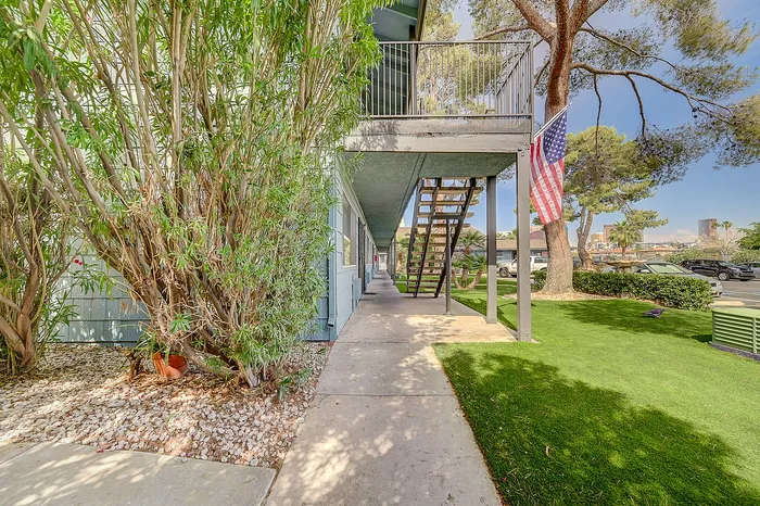 Inviting apartment exterior with lush greenery and American flag, featuring a charming walkway and stair access.