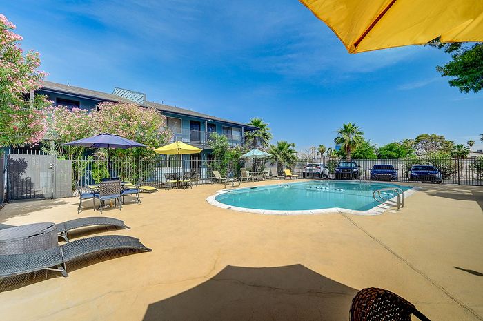Inviting apartment pool area with lush greenery, vibrant umbrellas, and sun loungers, perfect for relaxation.