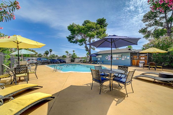 Inviting outdoor pool area with stylish patio furniture and vibrant umbrellas, surrounded by lush greenery under a bright blue sky.