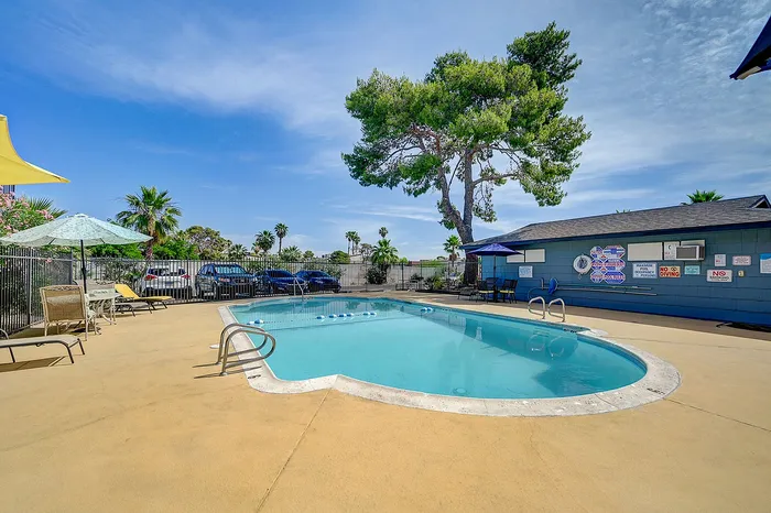 Inviting outdoor swimming pool with lounge chairs, umbrellas, and lush greenery under a clear blue sky.