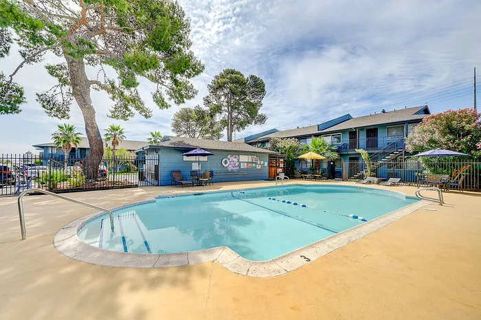 Inviting apartment complex featuring a pristine swimming pool surrounded by lush greenery and shaded seating, perfect for relaxation and outdoor enjoyment.