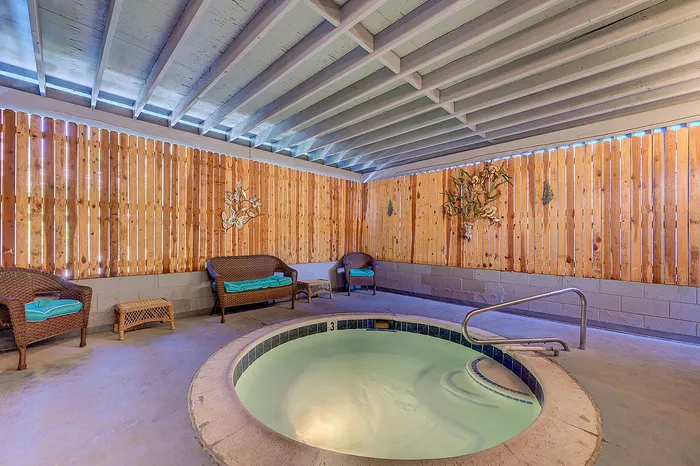 Inviting indoor spa area featuring a cozy hot tub, relaxed seating with wicker chairs, and elegant wooden decor.
