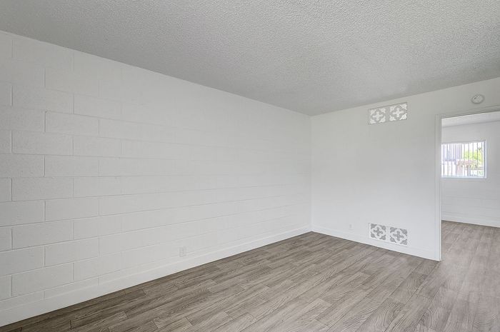 Bright and inviting room with white brick walls and stylish wood flooring, featuring ample natural light through a doorway.