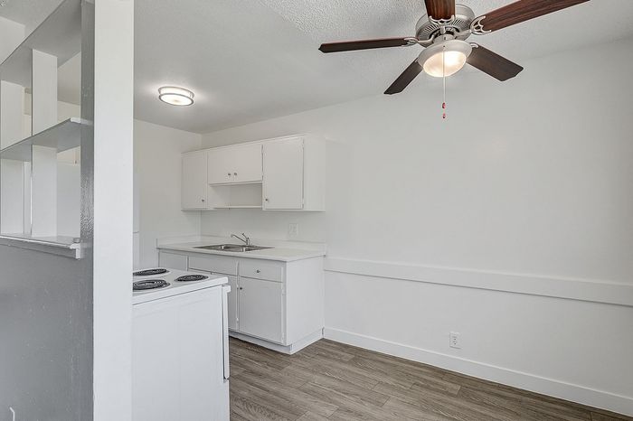 Sleek modern kitchen with white cabinets, elegant ceiling fan, and stylish wood flooring, perfect for contemporary living.
