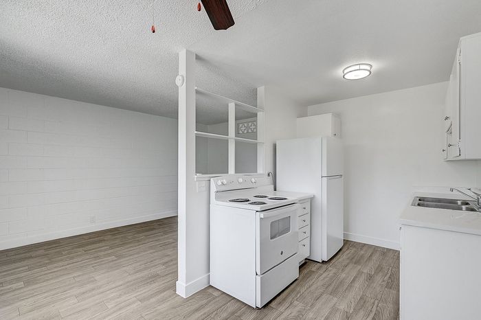 Bright and modern kitchen with white appliances, wood-style flooring, and open shelving for a spacious feel.