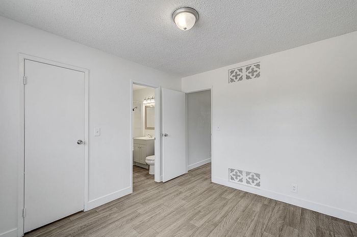 Bright room with elegant wood flooring, stylish ceiling light, and bathroom access, offering a seamless and modern living space.