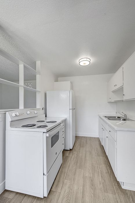 Bright and compact kitchen with modern white cabinetry, sleek appliances, and stylish wood flooring.