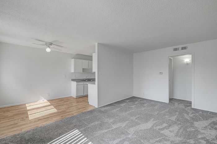 Bright and airy living space with an open-plan kitchen featuring modern white cabinetry and sleek countertops, complemented by elegant wood flooring and plush carpeting.