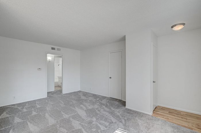 Bright, spacious room with plush carpeting and elegant white walls, leading to an inviting bathroom.