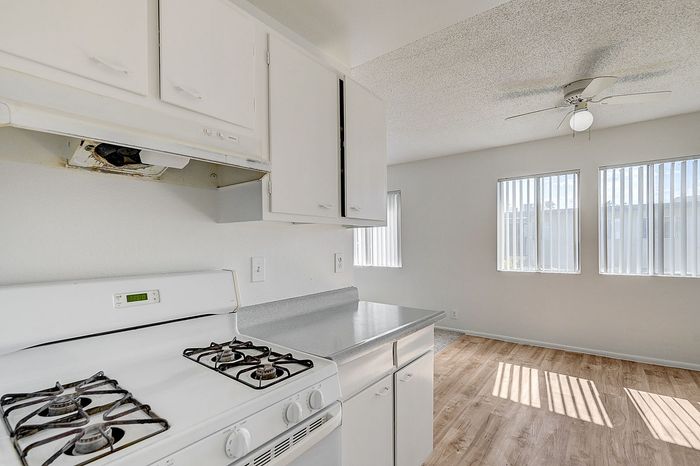 Bright kitchen with white cabinetry, modern gas stove, and a sunlit dining area with large windows and laminate wood flooring.