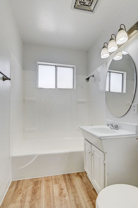 Bright and modern bathroom featuring elegant fixtures, a spacious bathtub, and chic wooden flooring.