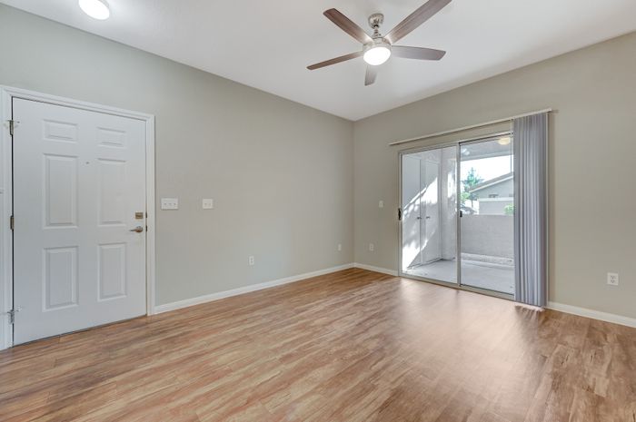 Bright and inviting living space with sleek wood flooring, ceiling fan, and sliding glass doors opening onto a cozy patio.