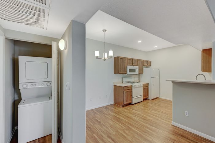 Modern apartment kitchen with stylish wooden cabinetry, sleek appliances, and an in-unit washer and dryer, offering convenience and elegance. Abundant natural light enhances the warm wooden flooring.