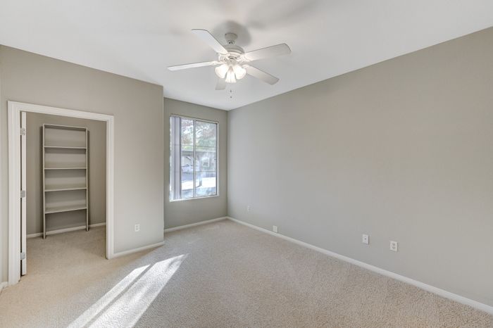 Bright and spacious bedroom with plush carpeting, large window, and built-in shelving, offering modern comfort and functionality.