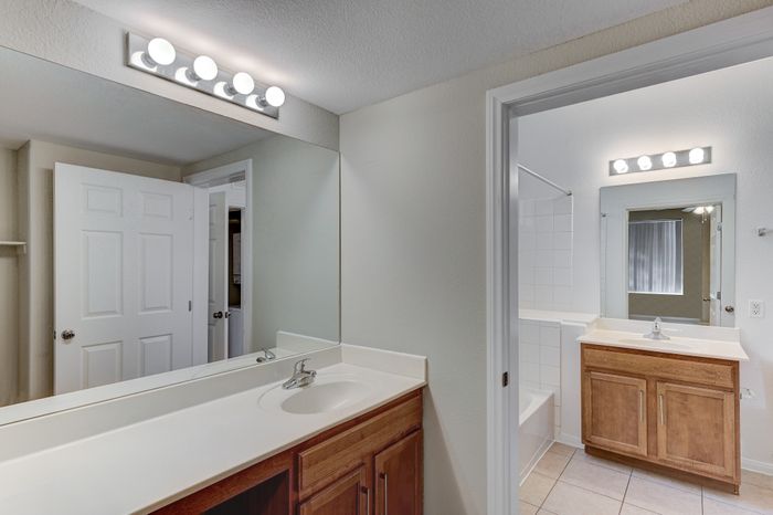 Bright, modern bathroom featuring double sinks, elegant light fixtures, and a spacious mirror with warm wood cabinetry.