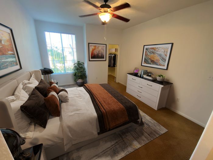 Elegant bedroom with plush bedding, stylish art, and a serene atmosphere enhanced by natural light and a ceiling fan.