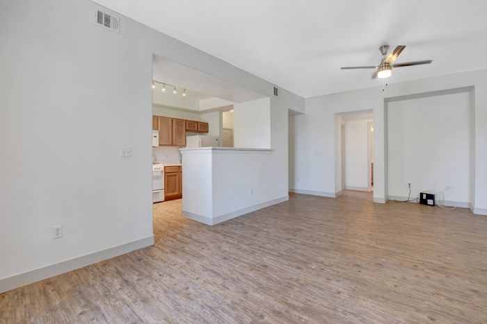 Bright modern living space with open layout, hardwood flooring, and stylish ceiling fan, leading to a cozy kitchen with wooden cabinets.