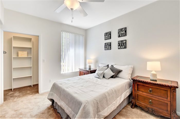 Inviting bedroom with cozy neutral tones, featuring a comfortable bed, stylish nightstands, and elegant wall decor. Natural light floods the room through large windows, enhancing the serene ambiance.