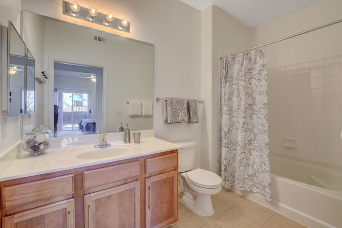 Bright and modern bathroom featuring elegant fixtures, wood cabinetry, and a chic shower curtain, with a view into a sunlit bedroom.