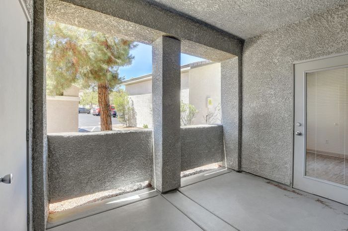 Charming outdoor patio space with textured walls, offering a serene view of surrounding trees and clear skies.