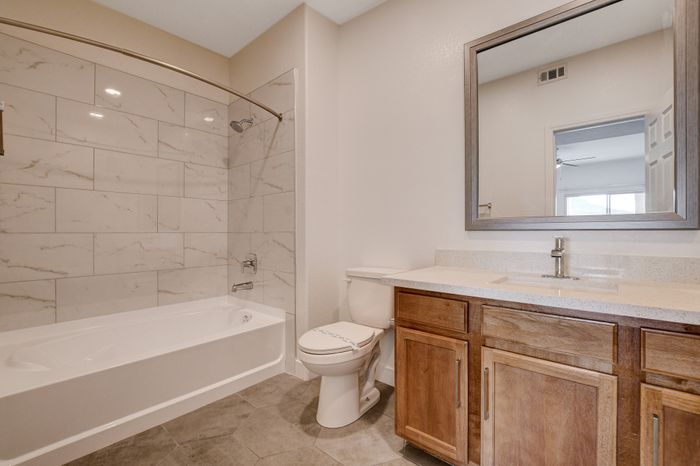 Elegant bathroom featuring a pristine bathtub, modern marble tiles, and a stylish wood-finished vanity with a large mirror.