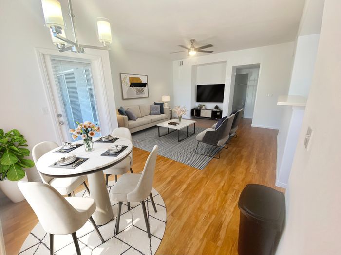 Modern open-concept living area with elegant dining table, cozy seating, and large TV, bathed in natural light and enhanced by stylish decor.