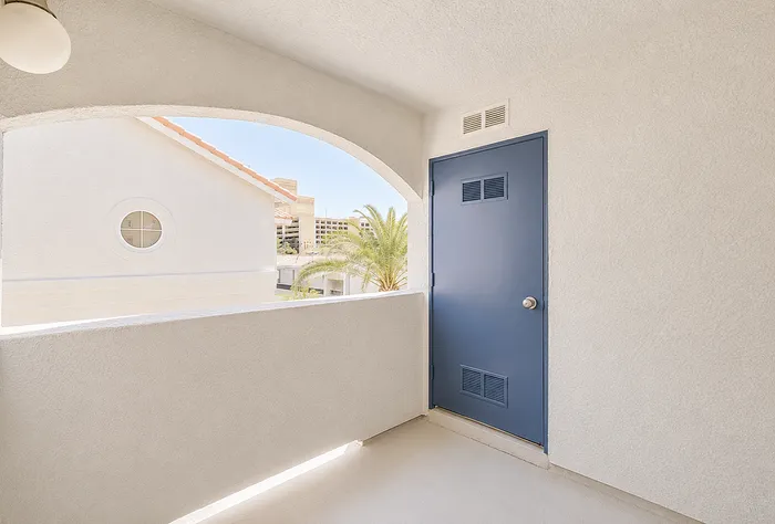 Bright and airy balcony with sleek blue door, offering a serene view of palm trees and modern architecture.