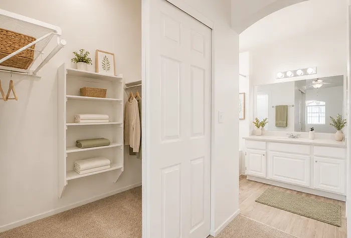Bright and elegant walk-in closet with pristine shelving, cozy carpet, and a modern bathroom featuring a sleek vanity and warm lighting.
