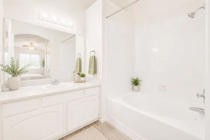 Bright and elegant bathroom featuring a spacious vanity, large mirror, and inviting bathtub, complemented by modern decor and fresh greenery.