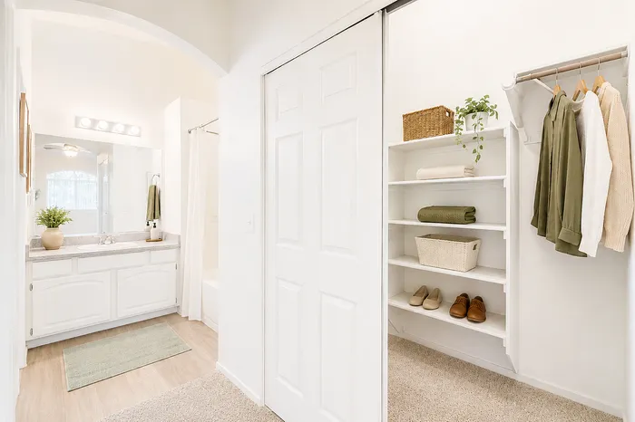 Bright and airy bathroom with elegant vanity, soft lighting, and built-in closet featuring organized shelves and hanging space.
