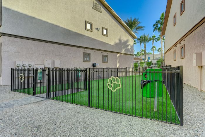 Charming fenced pet area with lush green artificial turf, perfect for residents and their furry friends, nestled between attractive apartment buildings with palm trees in the background.