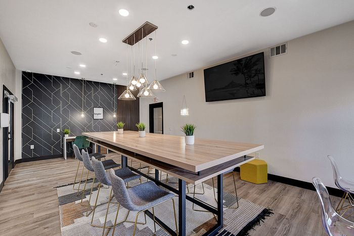 Chic and modern communal space featuring a long wooden table with pendant lighting, stylish seating, and vibrant decor accents.