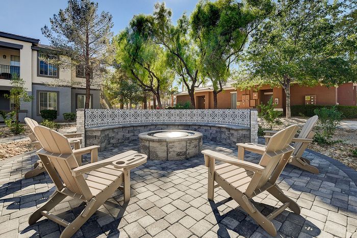 Charming outdoor patio with Adirondack chairs surrounding a stylish fire pit, set against a lush backdrop of trees in a serene apartment complex.