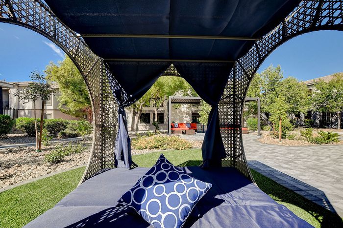 Luxurious outdoor patio with stylish canopy bed and vibrant landscaping in a serene setting.