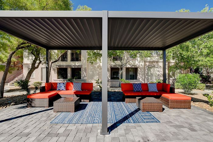 Chic outdoor lounging area with vibrant red seating, cozy cushions under a modern pergola, set against lush greenery and contemporary architecture.