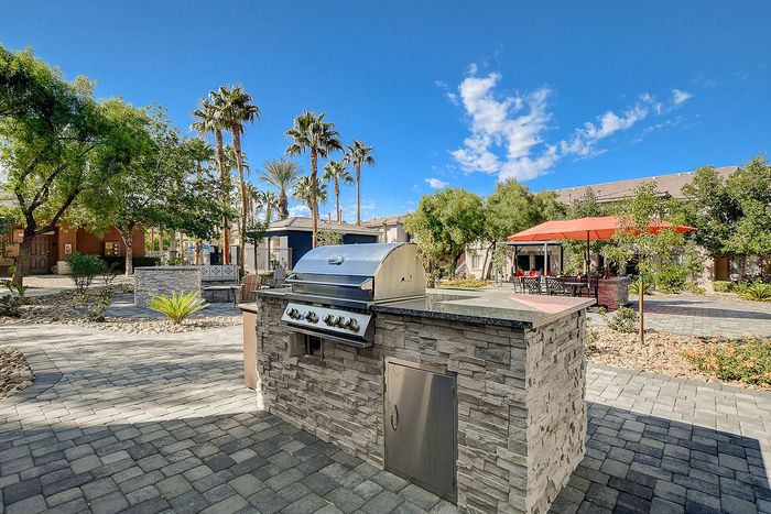 Charming outdoor barbecue area set amidst lush greenery and palm trees, featuring stylish stone design and spacious seating under vibrant umbrellas.
