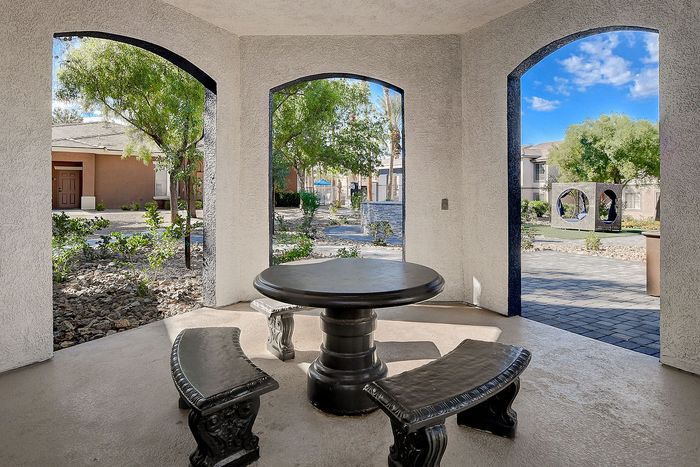 Charming outdoor patio with a round table and curved benches, surrounded by lush greenery and open archways, offering a tranquil retreat.