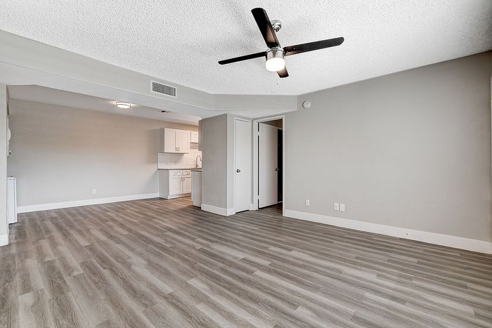 Elegant open-concept living space with modern flooring and a ceiling fan, leading to a sleek, white kitchen with contemporary cabinetry.