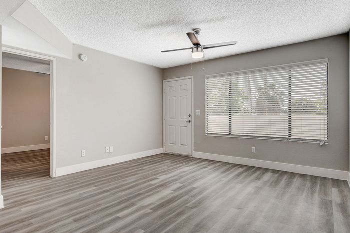 Bright and airy living room with modern flooring, large window, and ceiling fan in an inviting apartment space.