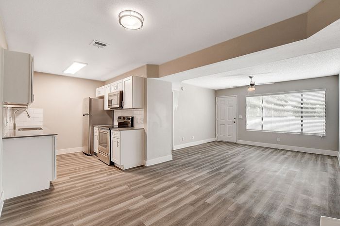 Modern apartment interior featuring a sleek kitchen with stainless steel appliances, open-concept living area with large window and wood-style flooring.