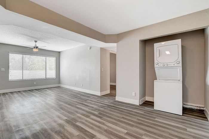 Modern apartment interior with open floor plan, featuring sleek wood flooring and abundant natural light from large windows, complete with an in-unit washer and dryer.